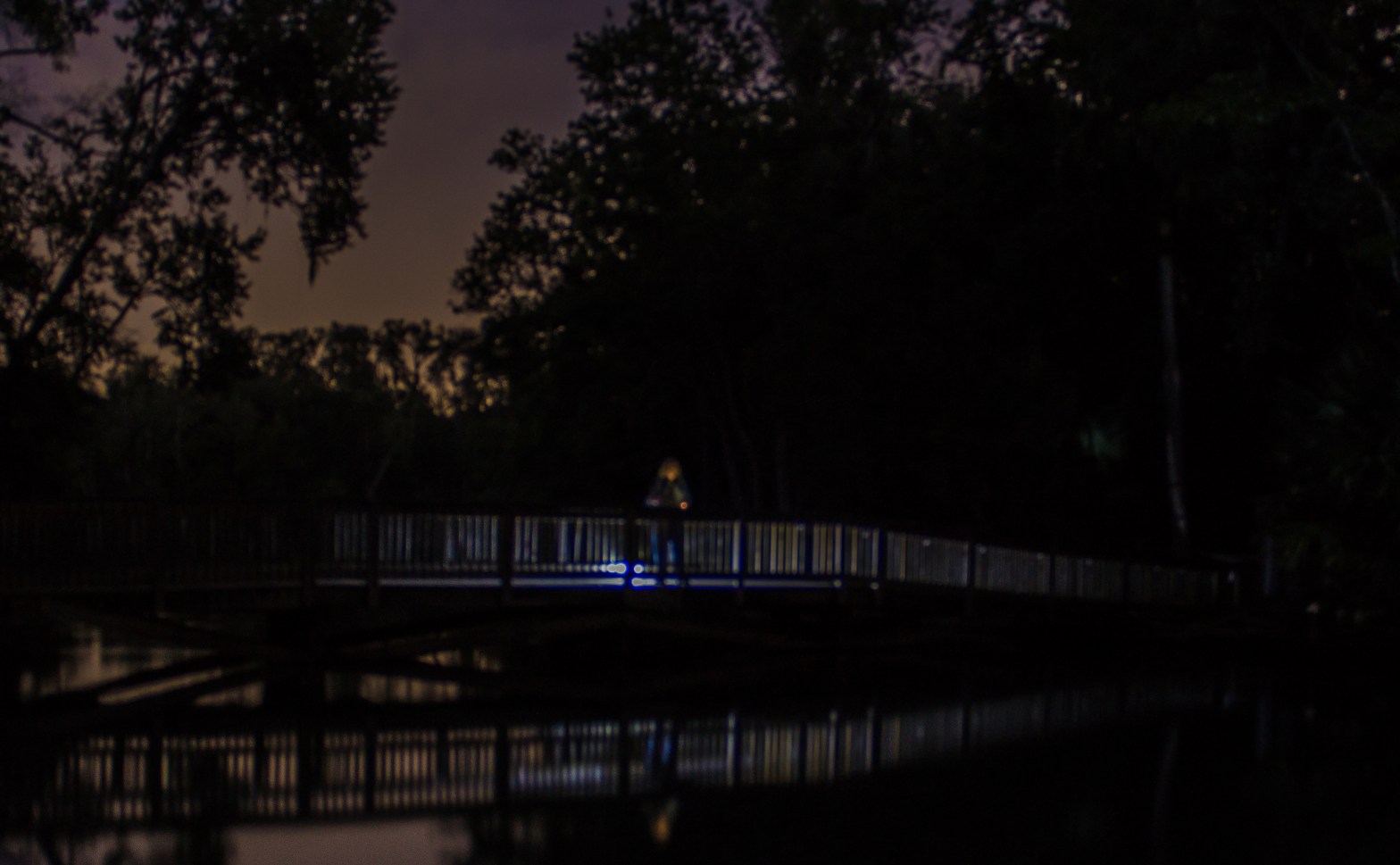 Man on bridge over calm springs at night with lantern light behind at feet